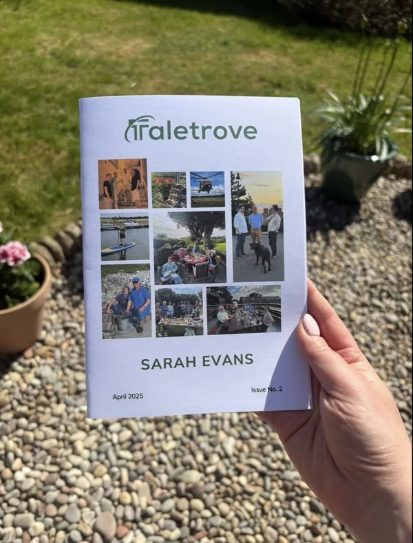 A hand holding a printed Taletrove newsletter with a photo collage cover